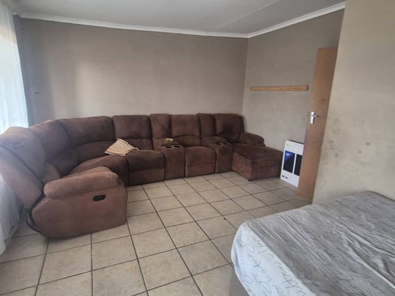 A living room featuring tiled flooring and a wall-mounted gas heater, currently showing signs of wear on the wall surfaces.