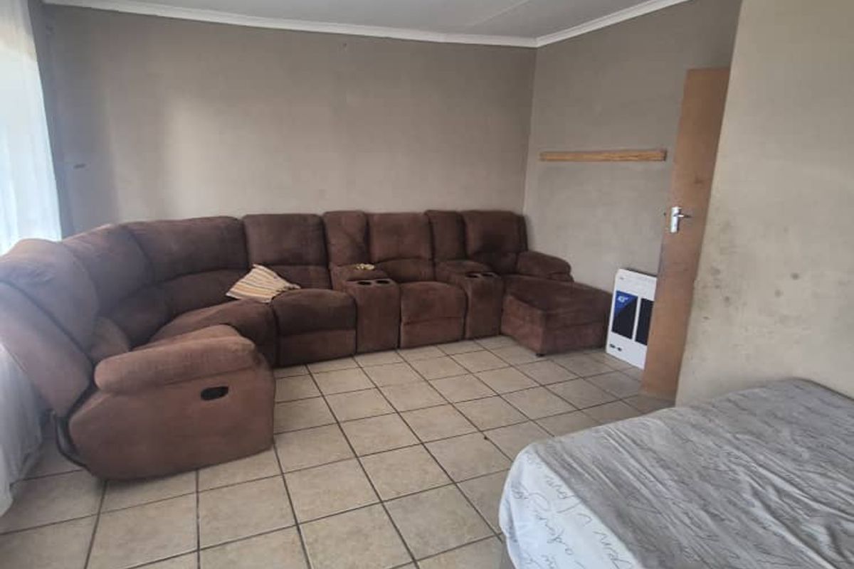 A living room featuring tiled flooring and a wall-mounted gas heater, currently showing signs of wear on the wall surfaces.