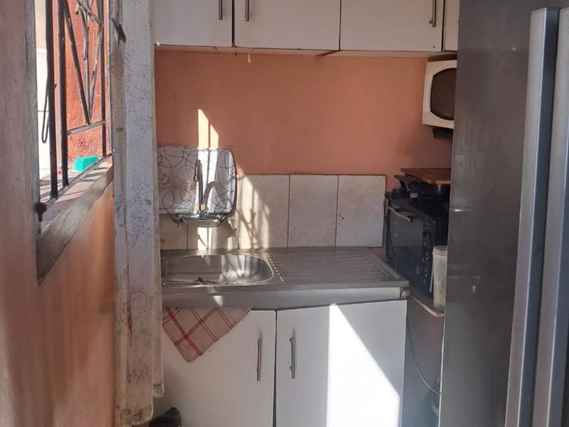 A compact scullery area featuring a stainless steel sink, tiled backsplash, and built-in white cabinetry, requiring some cosmetic updates.