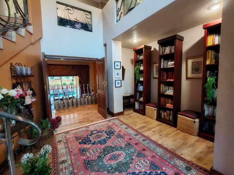 Spacious double-volume entrance hall featuring elegant wrought iron staircase detailing, built-in wooden bookshelves, and direct access to the rear patio area.