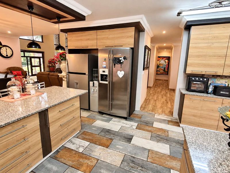 Modern open-plan kitchen featuring granite countertops, wood-finish cabinetry, a central island, and stylish pendant lighting, seamlessly flowing into the adjacent living area.