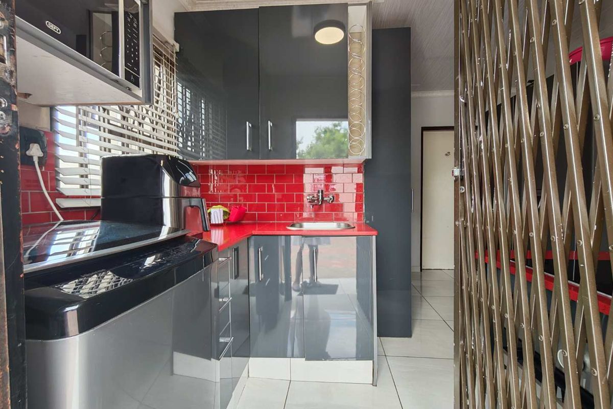 Compact kitchen featuring modern grey cabinetry, a vibrant red tiled backsplash, and tiled flooring, providing a functional and stylish prep area.
