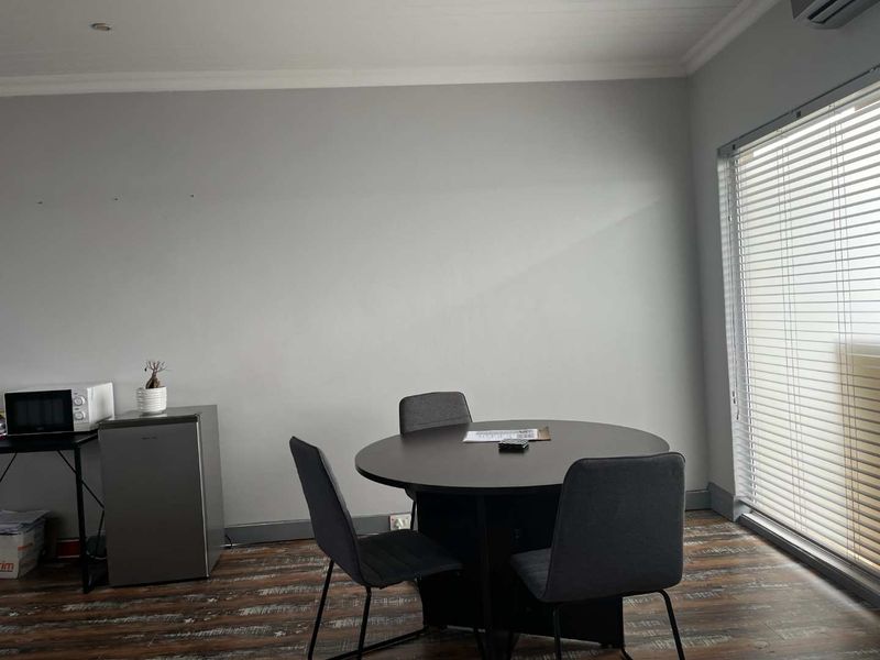 A functional living space featuring laminate flooring, recessed lighting, an air conditioning unit, and large windows fitted with venetian blinds.