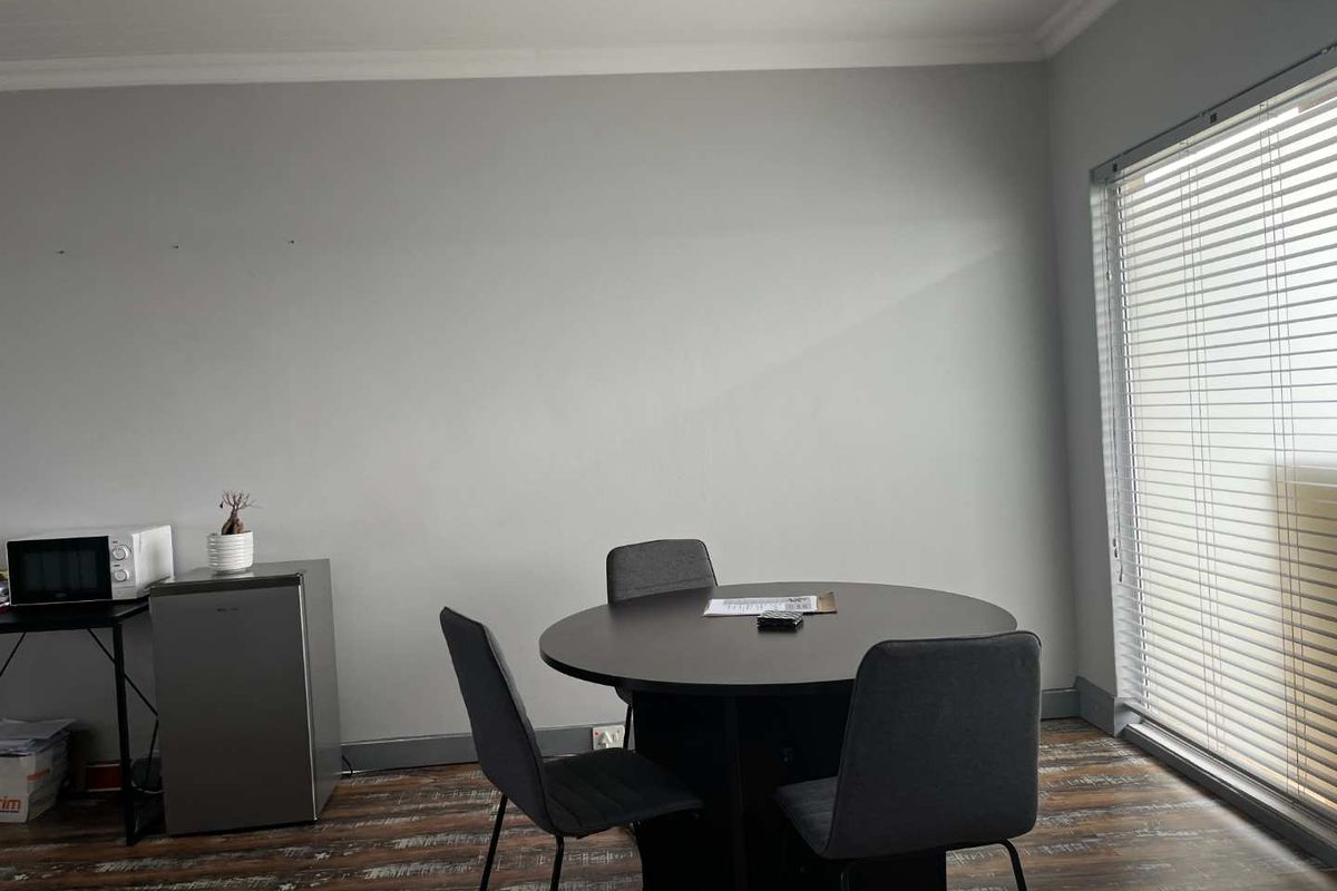 A functional living space featuring laminate flooring, recessed lighting, an air conditioning unit, and large windows fitted with venetian blinds.