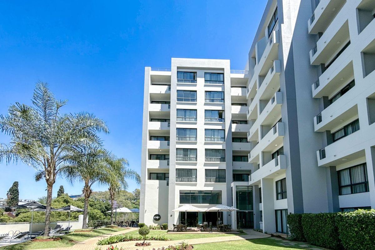 Exterior view of a modern multi-story apartment building featuring private balconies, landscaped gardens, and paved walkways.