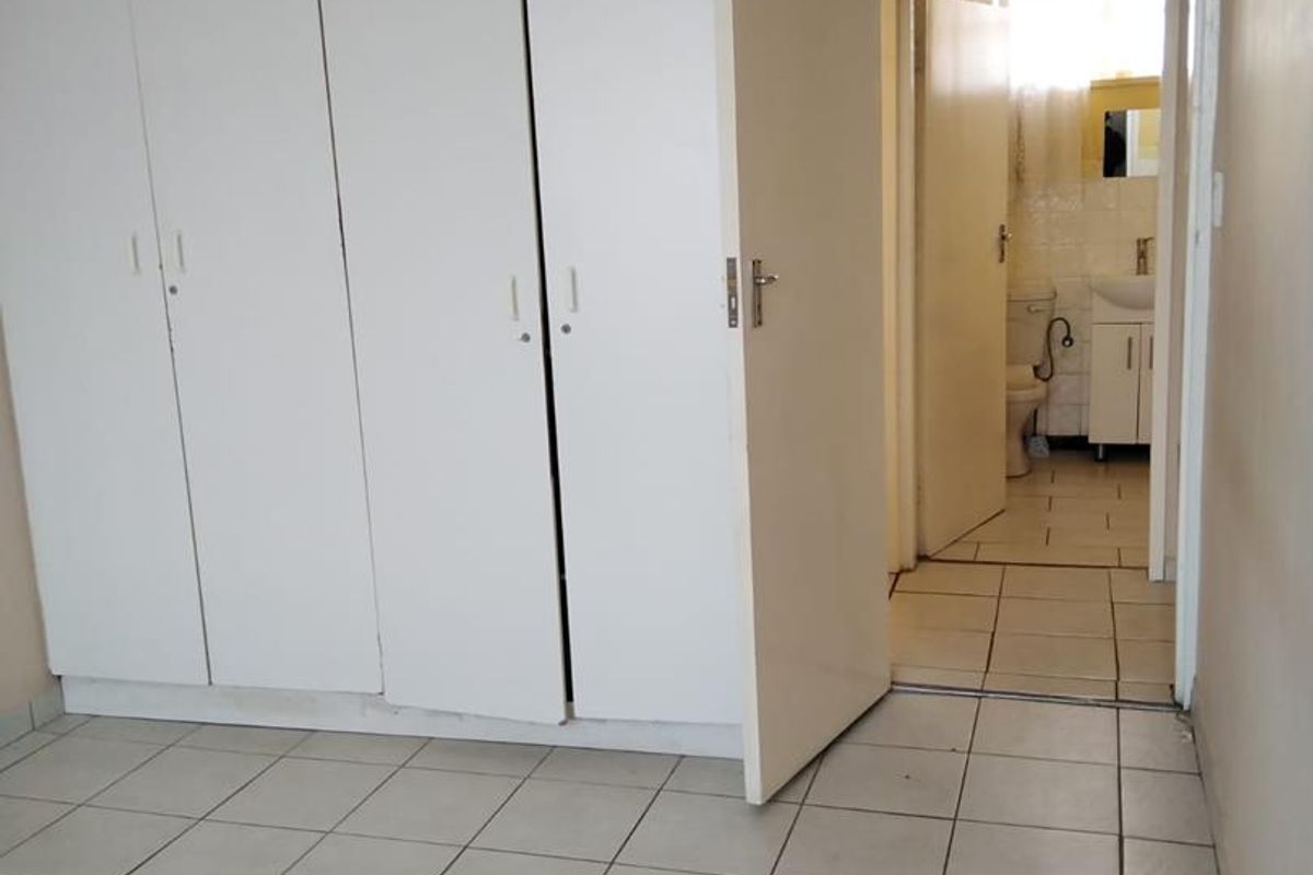 A bedroom featuring built-in cupboards and tiled flooring, with an adjoining bathroom visible through the doorway.