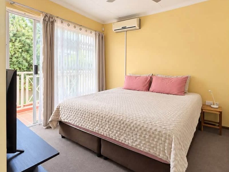 A well-lit bedroom featuring a ceiling fan, split-system air conditioning, and a sliding glass door providing access to an outdoor balcony area.
