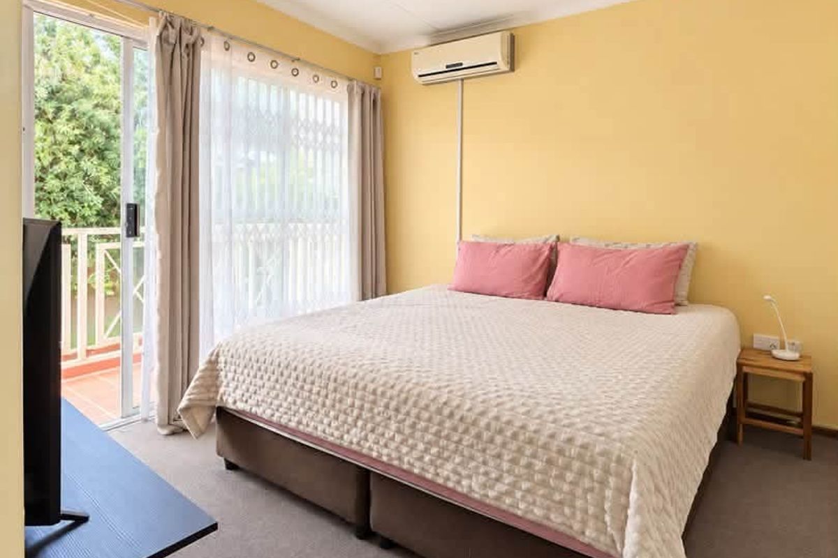 A well-lit bedroom featuring a ceiling fan, split-system air conditioning, and a sliding glass door providing access to an outdoor balcony area.