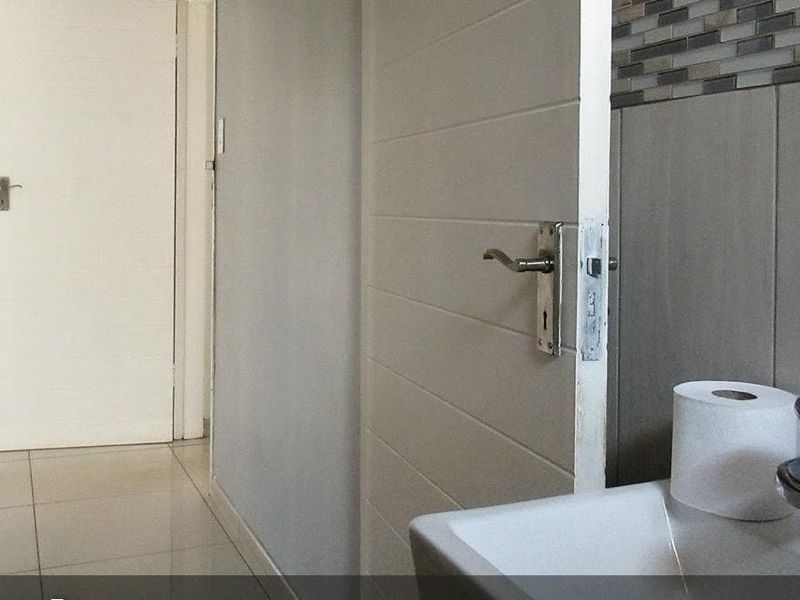 A clean, functional bathroom featuring tiled walls, a modern basin with a mixer tap, and neutral floor tiles.