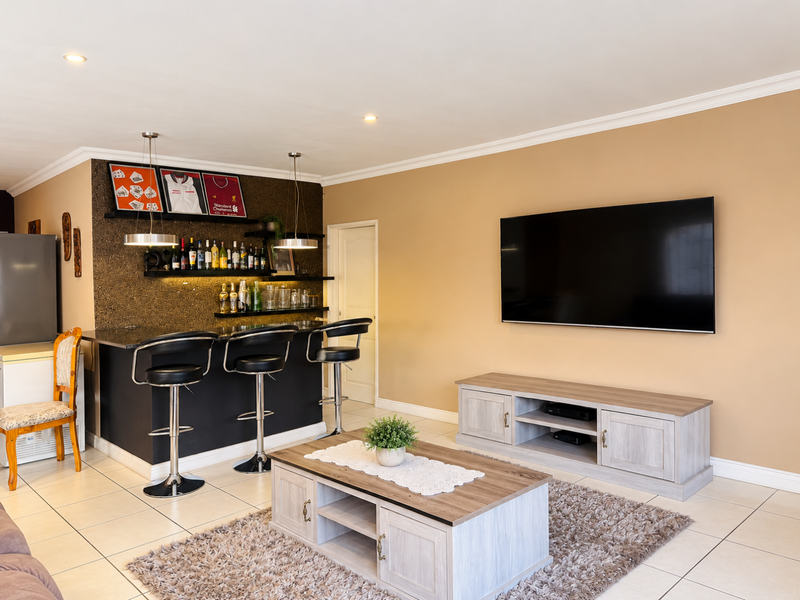A well-maintained living area featuring a dedicated built-in bar with integrated shelving, recessed lighting, and neutral tiled flooring throughout.