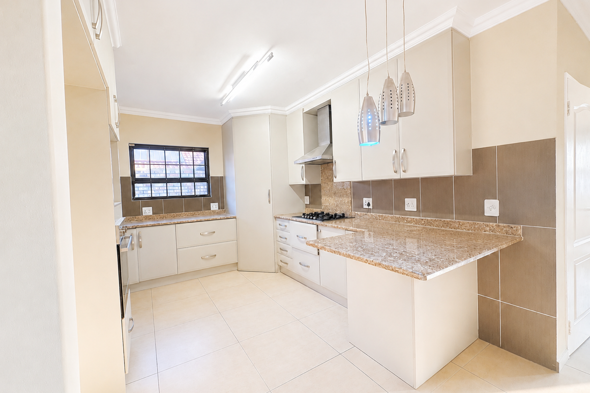 A clean, modern kitchen featuring granite countertops, built-in cabinetry, a gas hob with extractor fan, and neutral tiled finishes throughout.