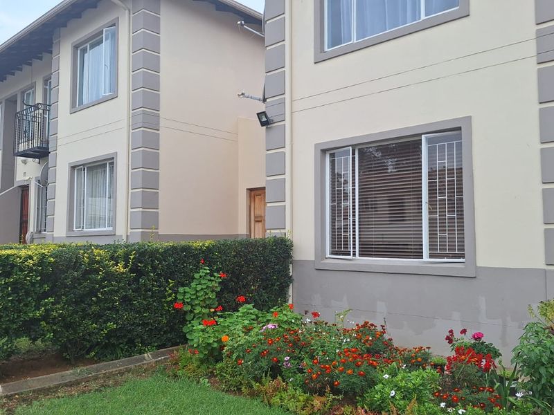 Exterior view of a multi-story apartment complex featuring cream-colored facades, sliding windows with security bars, and a well-maintained front garden.