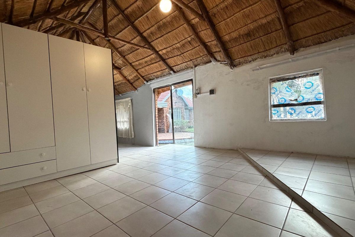 A bedroom featuring a traditional thatched roof with exposed rafters, tiled flooring, and a built-in wardrobe, offering a rustic cottage aesthetic.