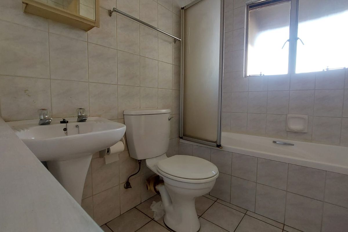 A dated bathroom featuring a pedestal basin, toilet, and a combined bathtub with a shower screen, finished with neutral wall and floor tiles.