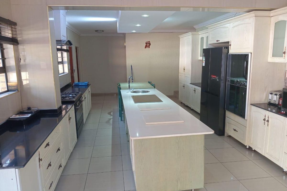 Spacious kitchen featuring a central island with a built-in sink, ample cabinetry, dark countertops, and integrated oven and hob appliances.
