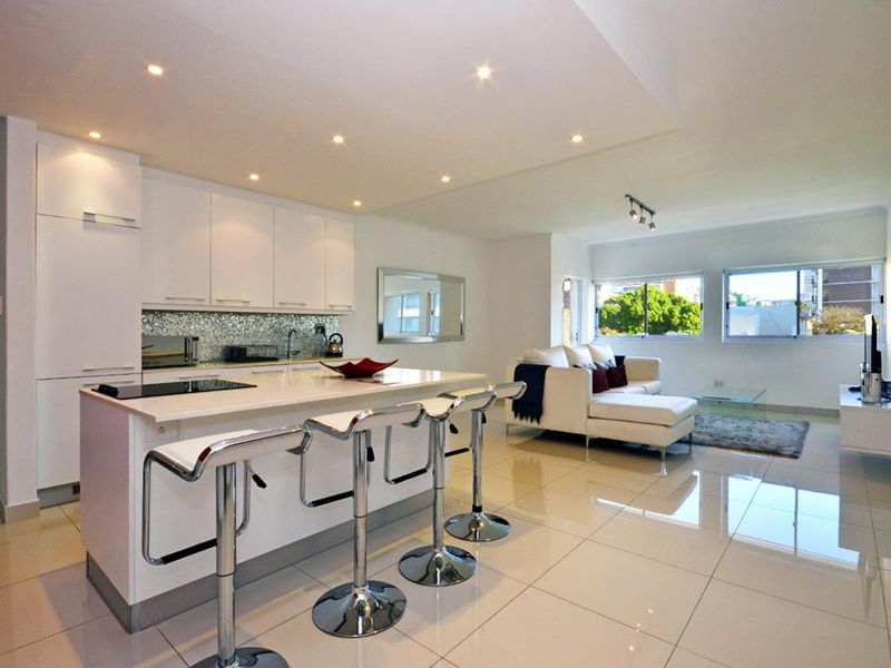 Modern open-plan living area featuring a sleek kitchen with a central island, mosaic backsplash, and polished tiled flooring throughout the bright, connected space.