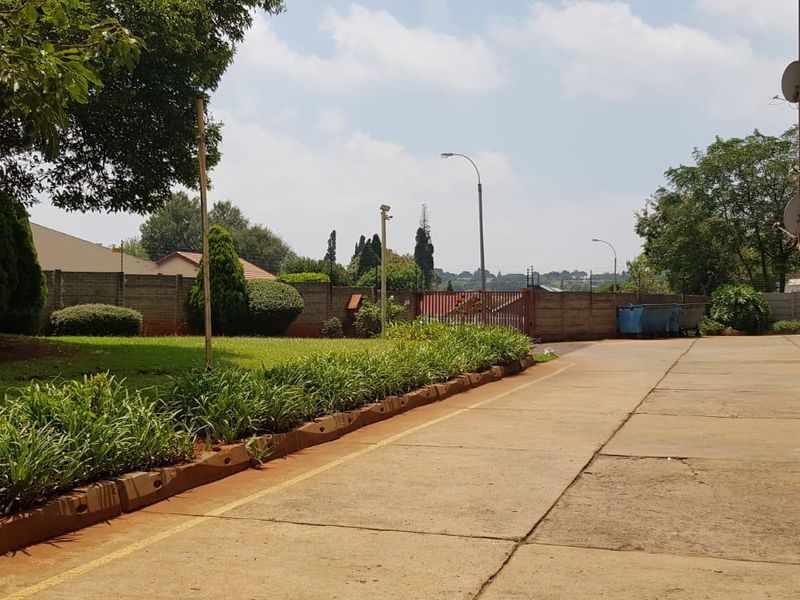 View of the apartment complex exterior featuring a concrete driveway, landscaped garden area, and perimeter boundary wall.