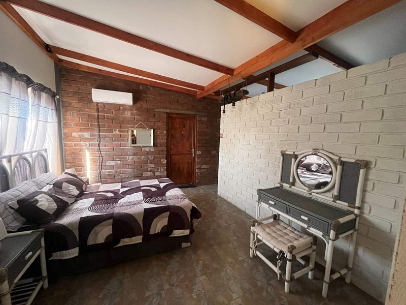 A rustic bedroom featuring exposed brick walls, timber ceiling beams, tiled flooring, and a split-system air conditioner.