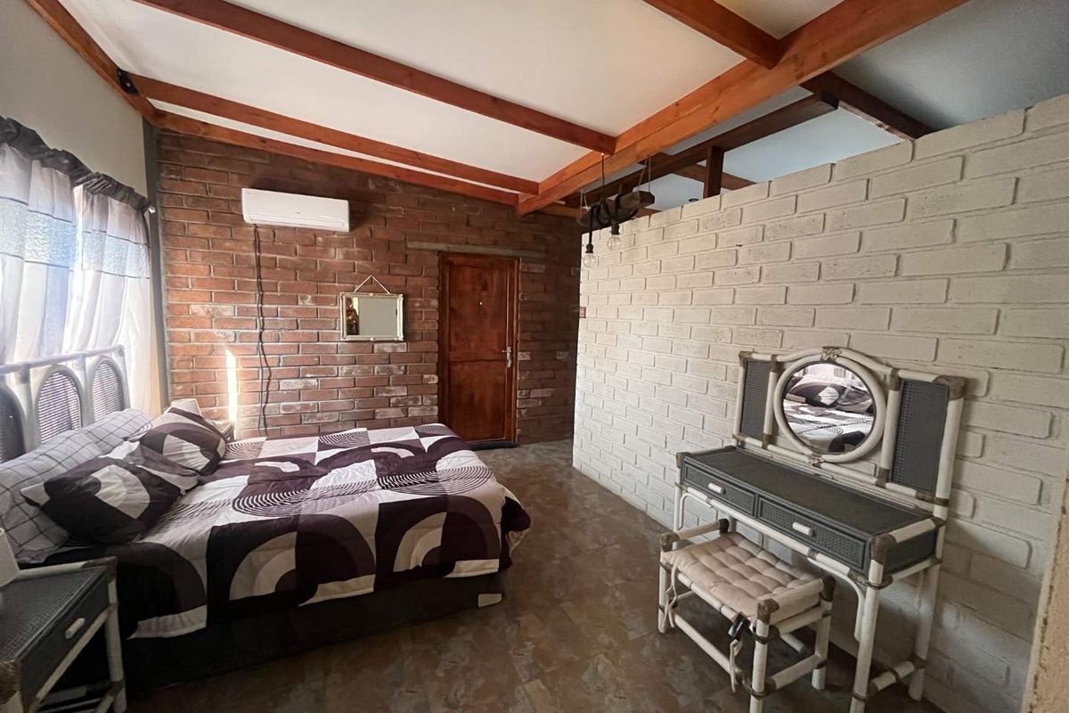A rustic bedroom featuring exposed brick walls, timber ceiling beams, tiled flooring, and a split-system air conditioner.