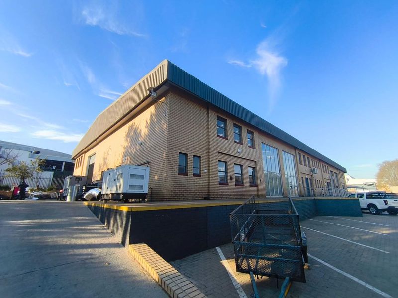 Industrial warehouse building featuring a brick facade, metal roofing, and a dedicated loading dock area with paved parking.