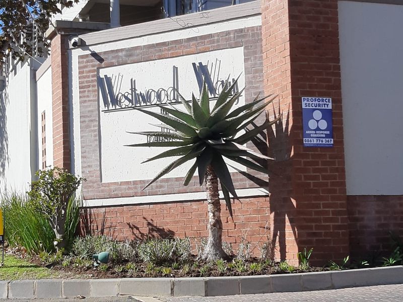 The front entrance facade of Westwood Way townhouse complex featuring brick masonry, security signage, and perimeter electric fencing.