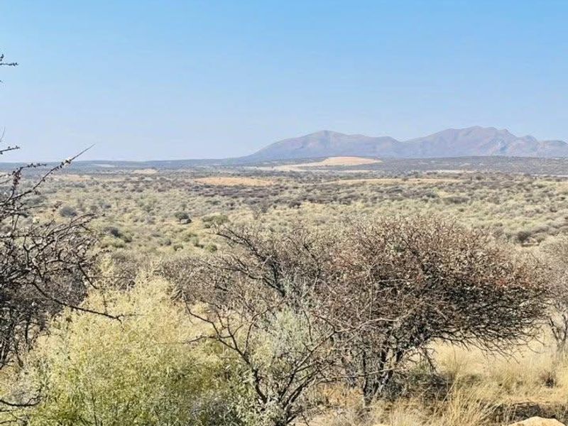 A scenic landscape view overlooking expansive natural terrain with distant mountain ranges under a clear blue sky.