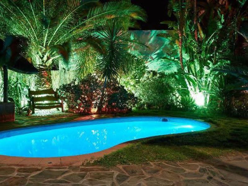 A beautifully illuminated outdoor swimming pool area at night, featuring stone paving and lush garden landscaping.