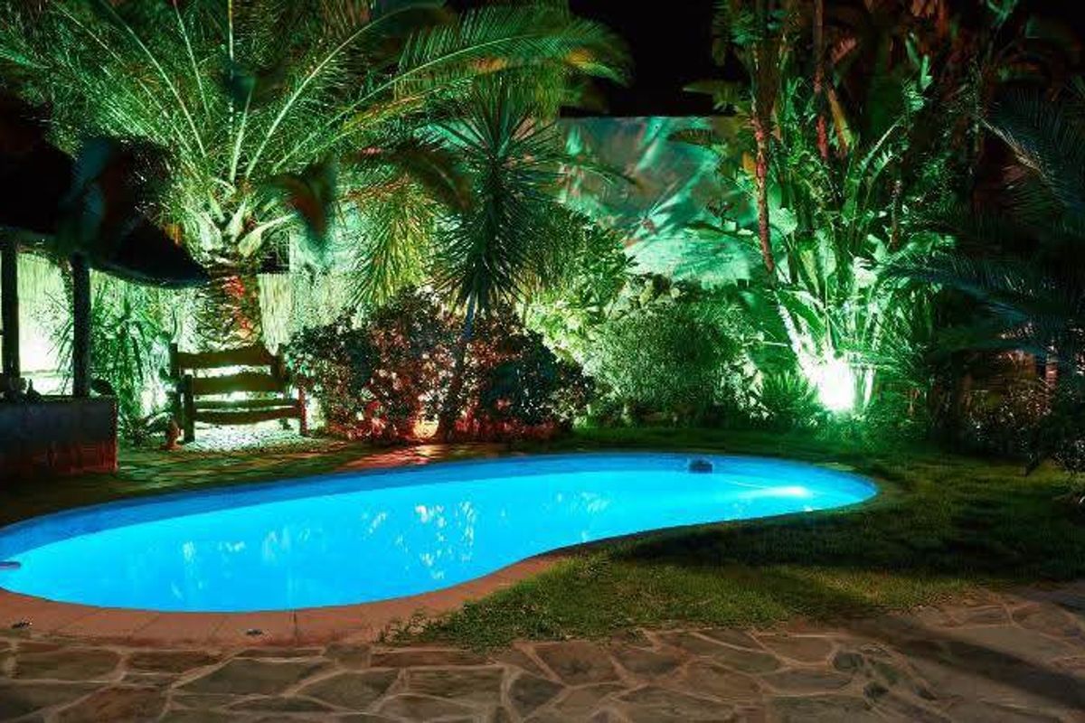 A beautifully illuminated outdoor swimming pool area at night, featuring stone paving and lush garden landscaping.