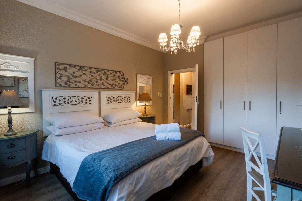 A well-maintained bedroom featuring built-in floor-to-ceiling wardrobes, crown molding, and a classic chandelier, offering a comfortable and functional living space.