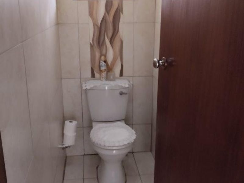 A compact bathroom featuring floor-to-ceiling tiling, a standard toilet, and a small window with security bars.