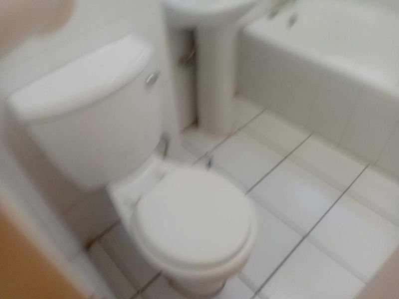 A compact bathroom featuring a standard toilet, pedestal basin, and bathtub with tiled flooring.