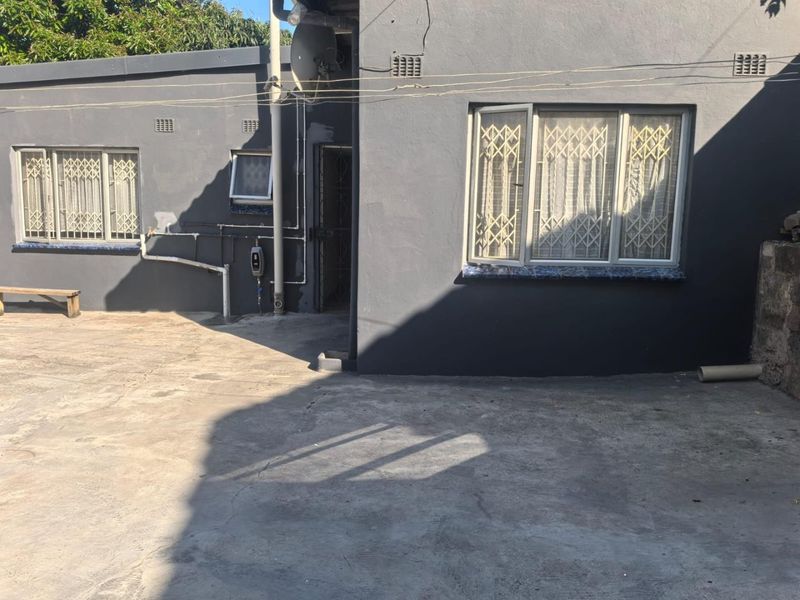 Rear exterior view of the property featuring concrete paving, security gates on windows, and exposed external utility infrastructure.