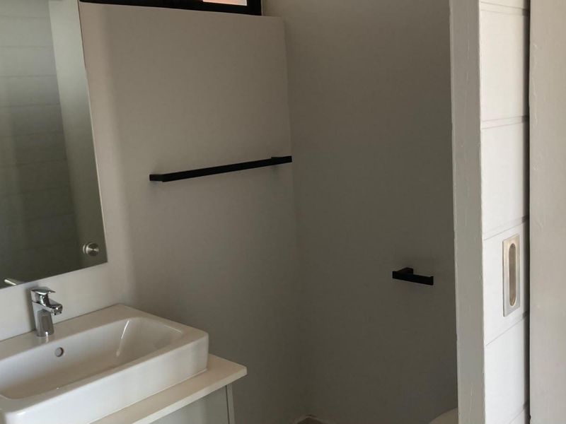 A clean, modern bathroom featuring a vanity basin with chrome mixer tap, wall-mounted mirror, and matte black hardware fixtures.