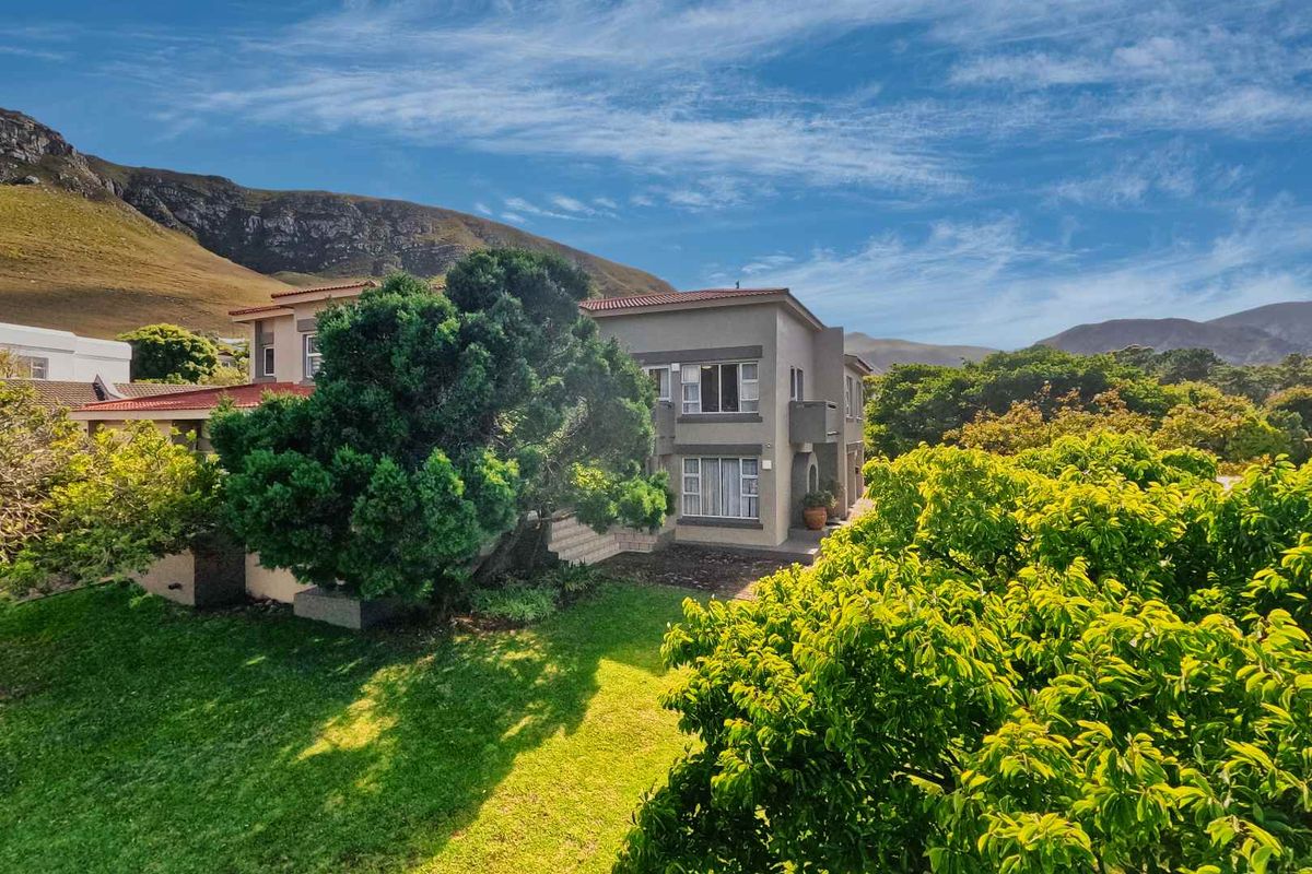 A view of the rear elevation of the house, featuring a landscaped garden, mature trees, and mountain backdrop.