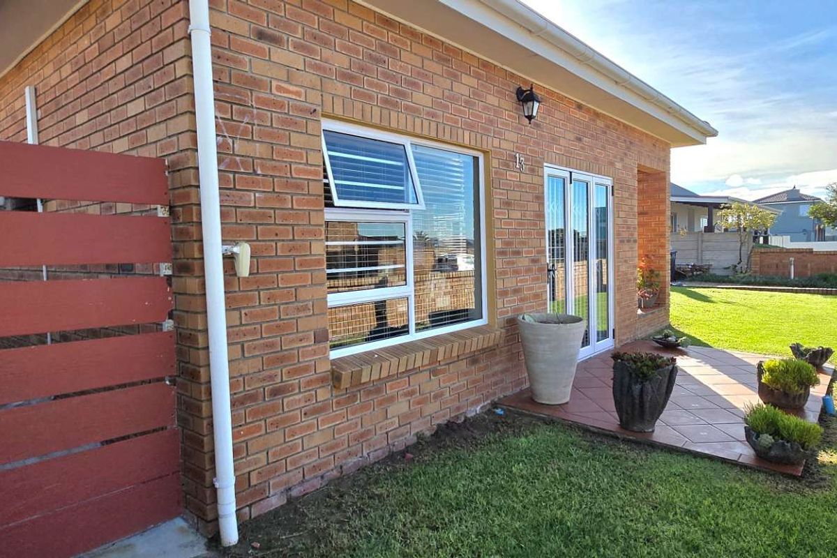 A side view of the brick house featuring a tiled patio area, large windows, and a well-maintained lawn.