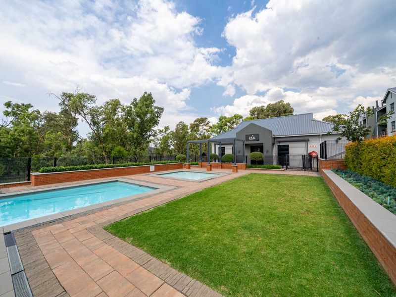 Well-maintained communal pool area featuring a swimming pool, spa, paved surround, and landscaped lawn set against a modern building facade.