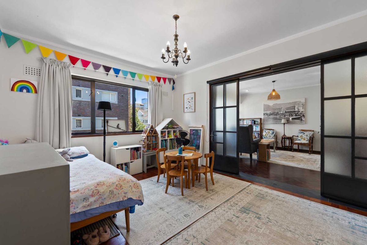 Spacious bedroom featuring timber flooring, a classic chandelier, and large sliding glass doors that connect to an adjacent living area.