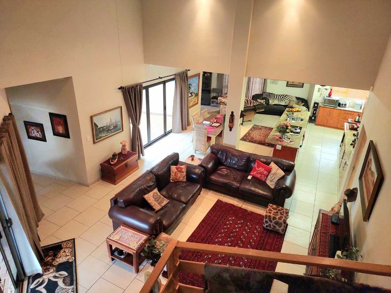 Spacious open-plan living area featuring a double-volume ceiling, tiled flooring, and a functional kitchen with a central island and integrated cabinetry.
