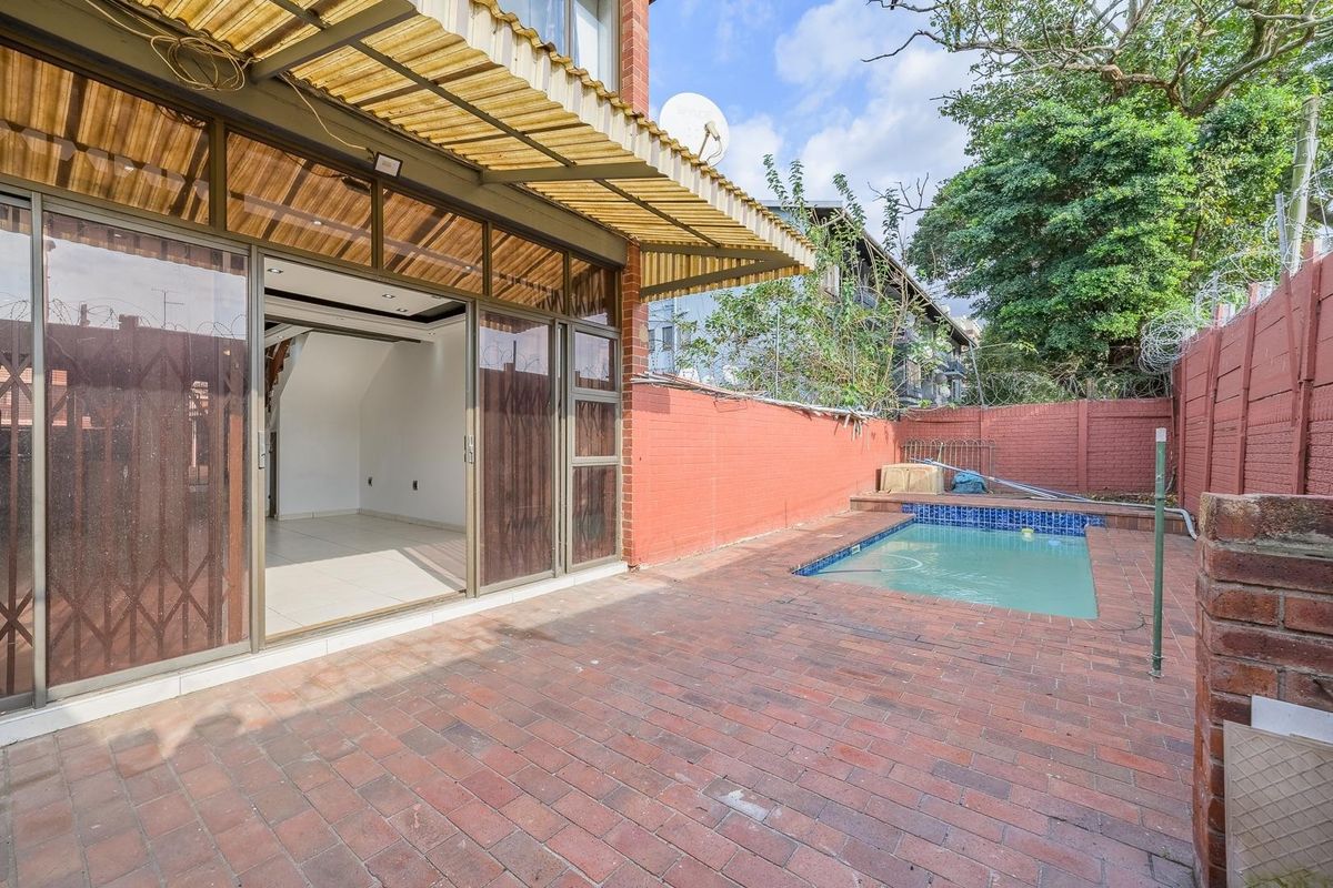 Rear exterior view featuring a private swimming pool, brick-paved patio area, and sliding door access to the main living space.