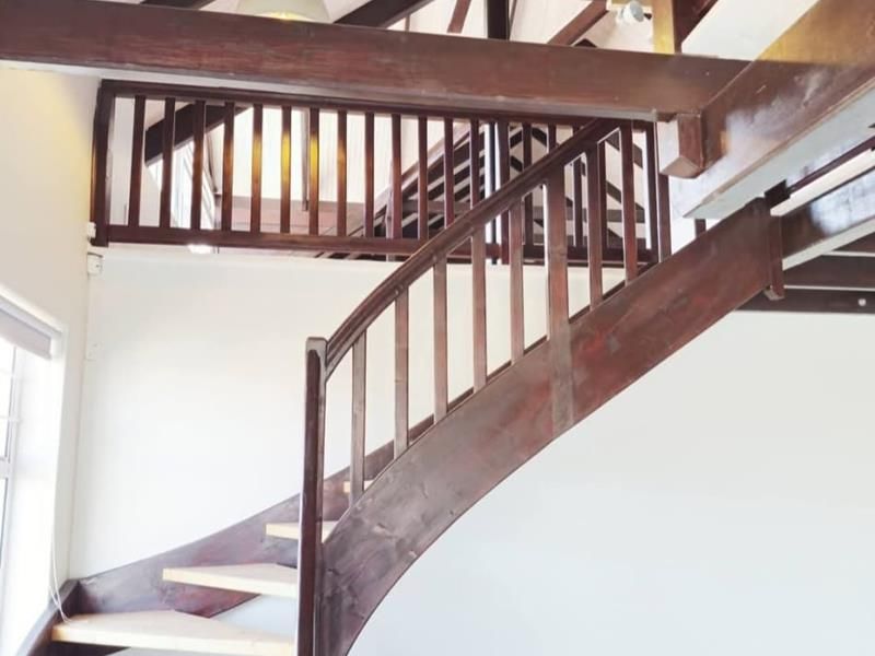 Spacious living area featuring a striking timber staircase, vaulted ceilings with exposed beams, and a mezzanine level overlooking the main floor.