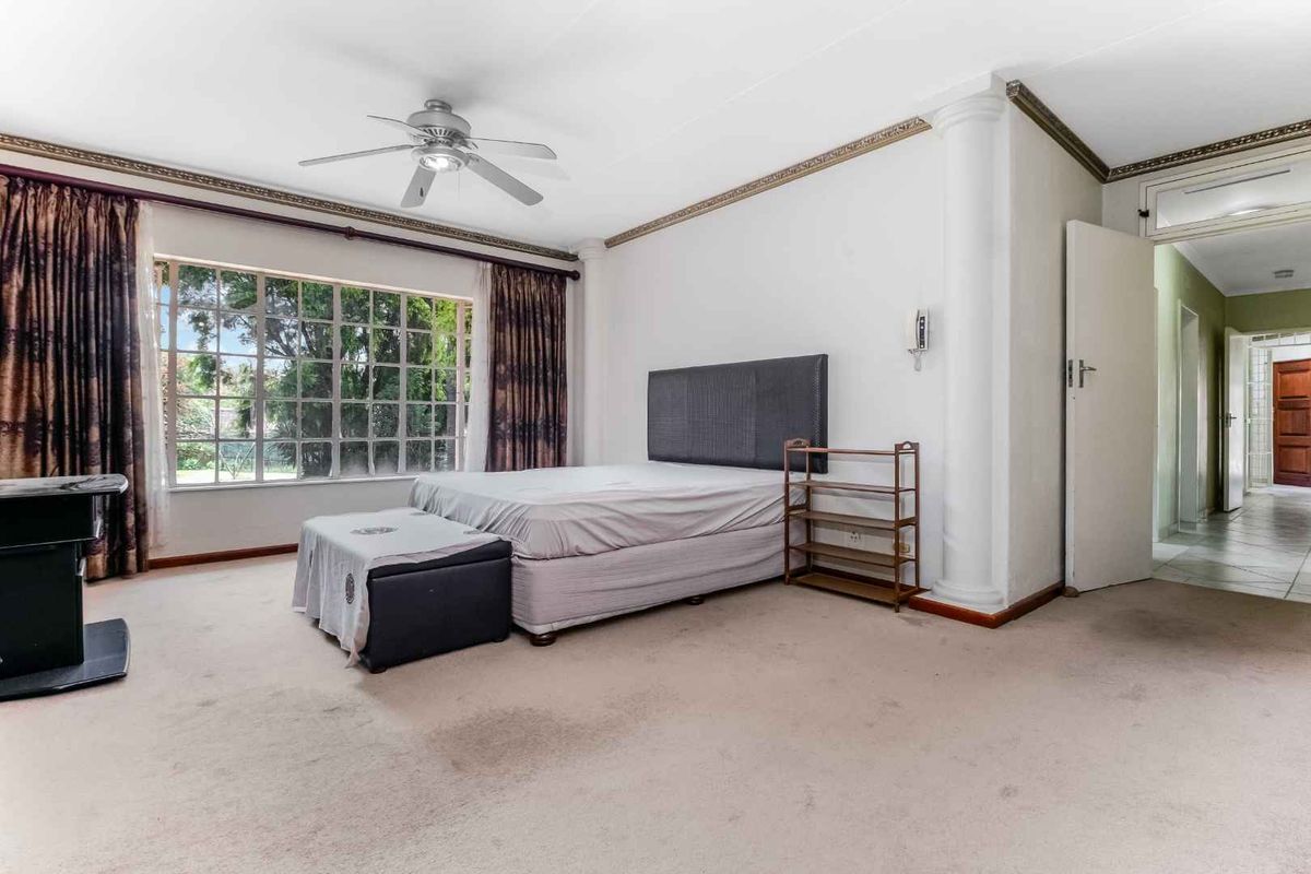 Spacious bedroom featuring a large window, ceiling fan, decorative crown molding, and a column detail, offering a neutral canvas for personalization.