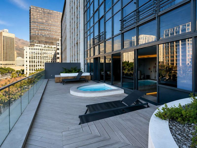 Spacious modern balcony featuring timber decking, a built-in spa, glass balustrades, and expansive city views through floor-to-ceiling sliding glass doors.