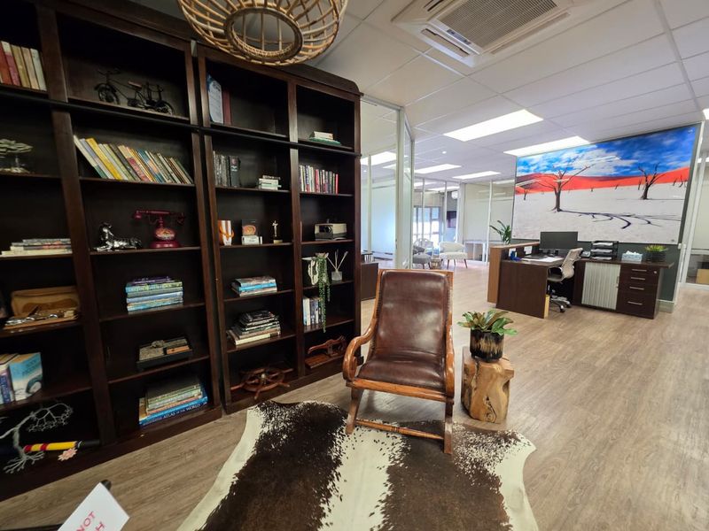A professional office space featuring built-in dark wood shelving, glass partitions, and modern recessed ceiling lighting with a clean, functional layout.