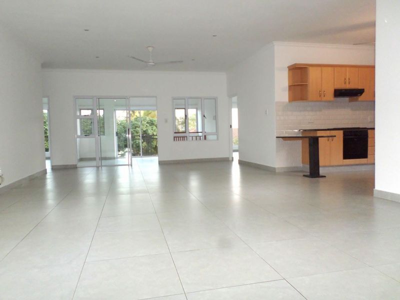 Spacious open-plan living area featuring large format floor tiles, recessed lighting, and a functional kitchen with built-in cabinetry and appliances.