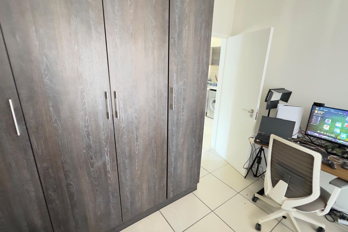 A bedroom featuring dark wood-finish built-in wardrobes and light-colored floor tiles, with a doorway leading to an adjacent utility area.