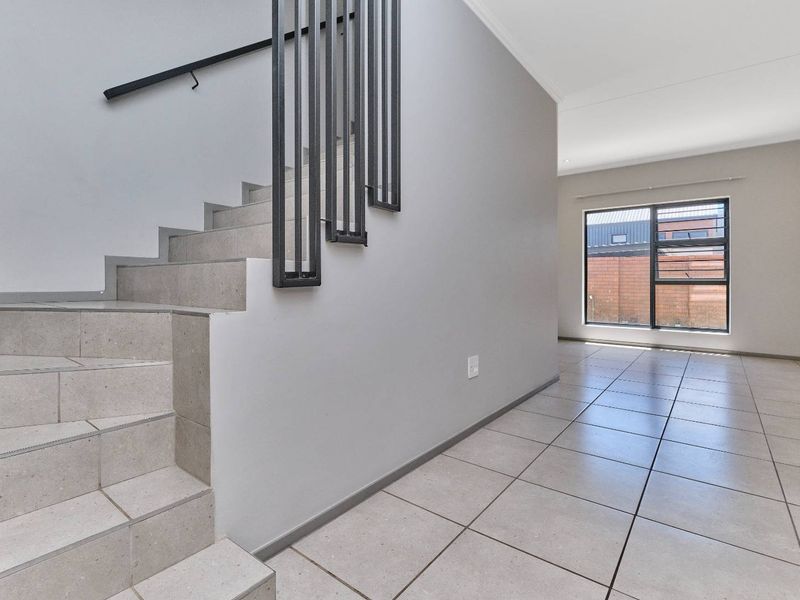 Bright entrance hall featuring a tiled staircase with a modern metal balustrade, leading into an open-plan living area with large windows.