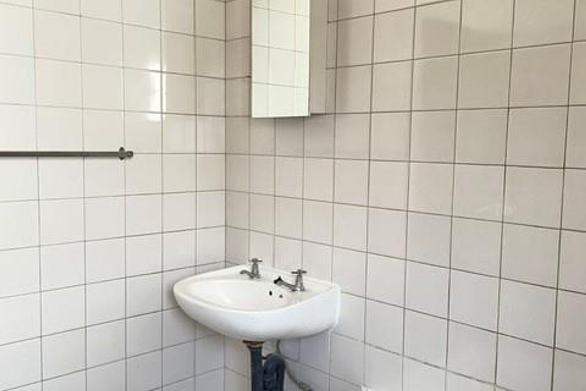 A functional bathroom featuring a wall-mounted basin, bathtub, and tiled finishes, offering a blank canvas for modernization and cosmetic updates.