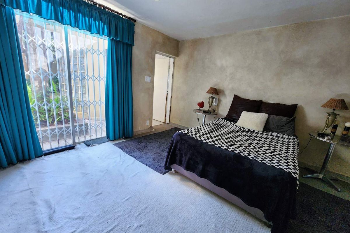 Spacious bedroom featuring a sliding glass door with security gate, ceiling fan, and direct access to an outdoor area.