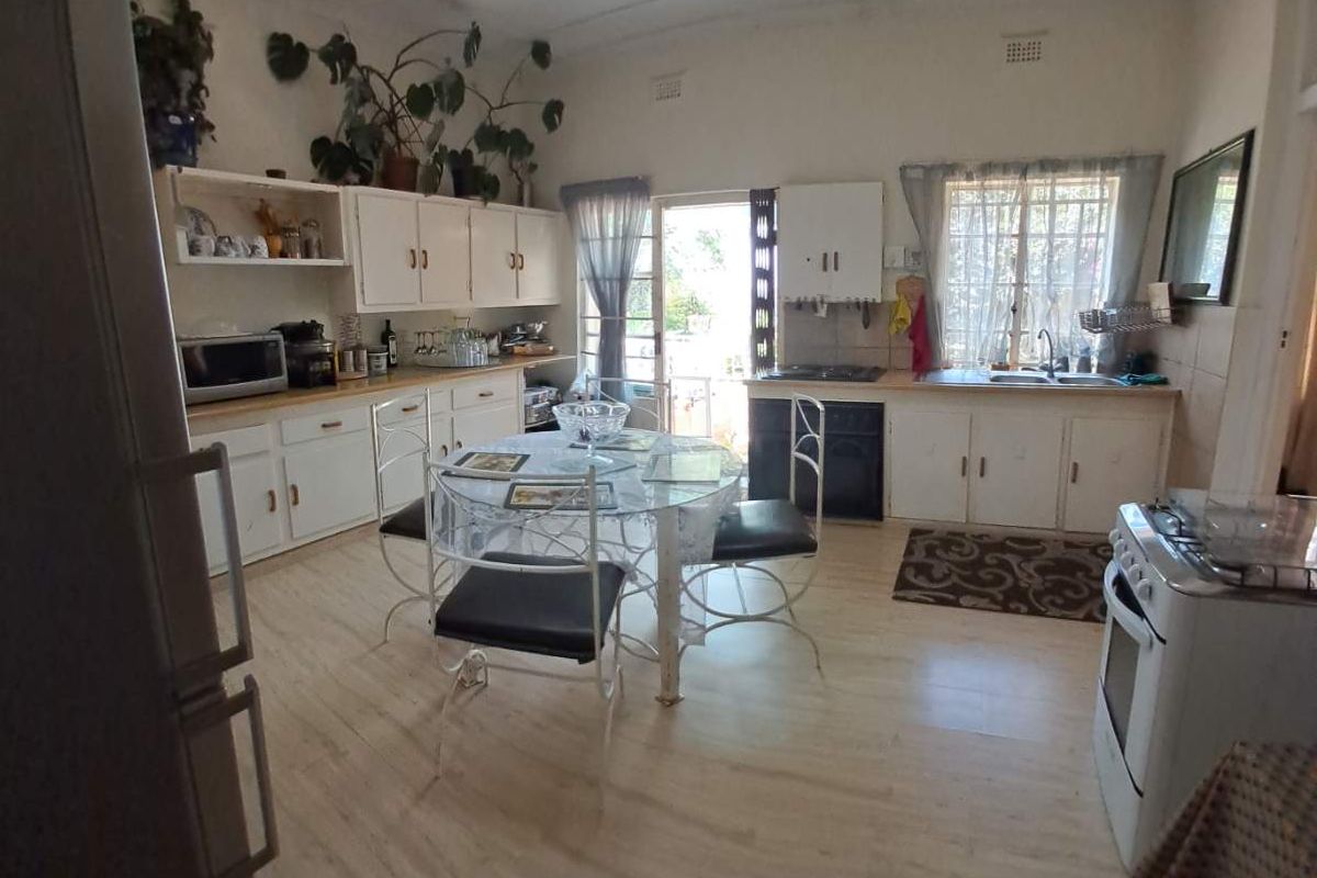 A dated kitchen featuring white cabinetry, laminate flooring, and a dining area with direct access to the exterior.