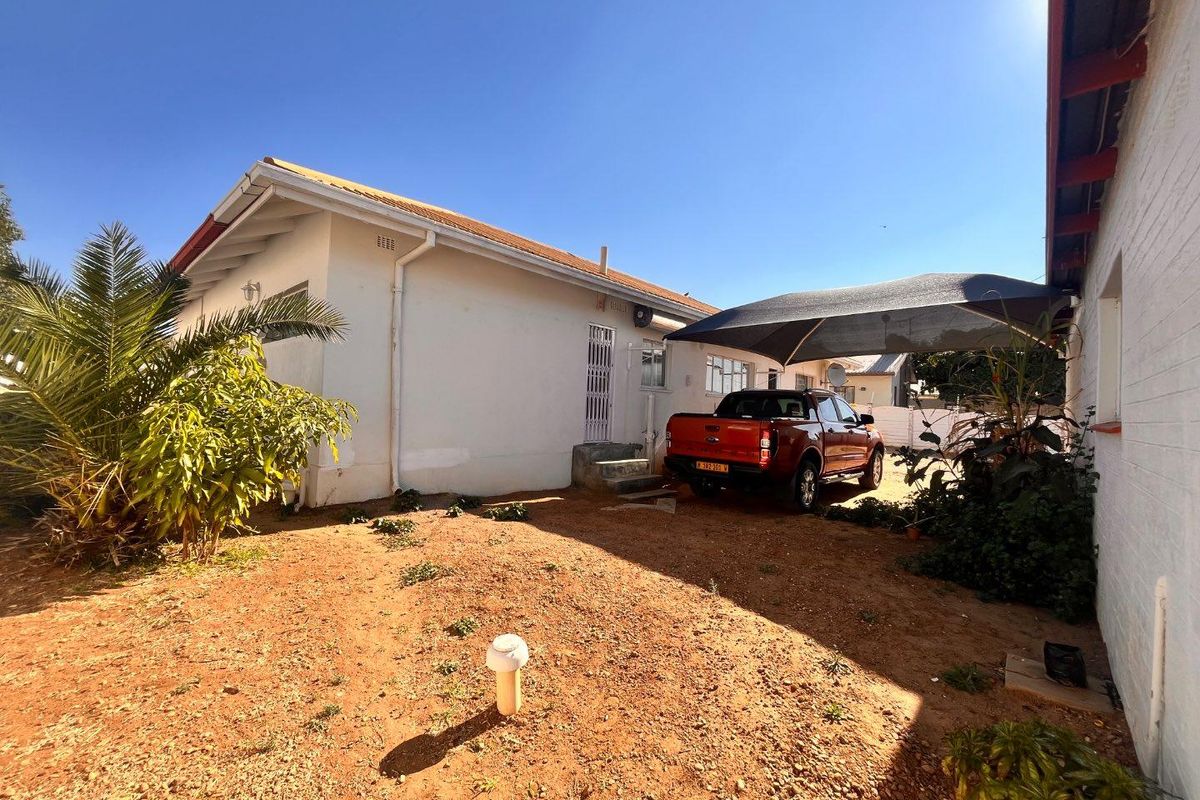 Rear exterior view of the property featuring a gravel yard, shade sail parking area, and white painted brick walls.